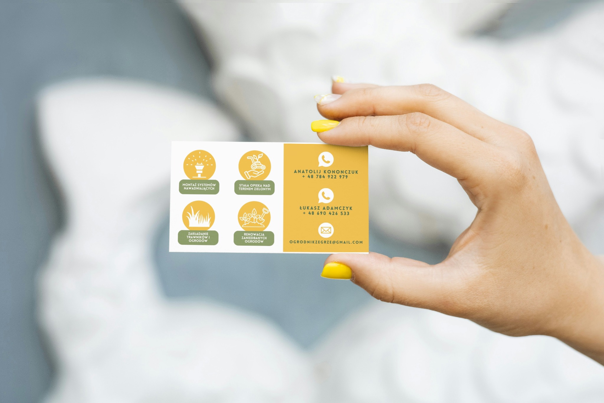 Dłoń z żółtym manicure trzyma wizytówkę firmy ogrodniczej z ikonami usług: nawadnianie, opieka, zakładanie trawników, renowacja ogrodów i danymi kontaktowymi.