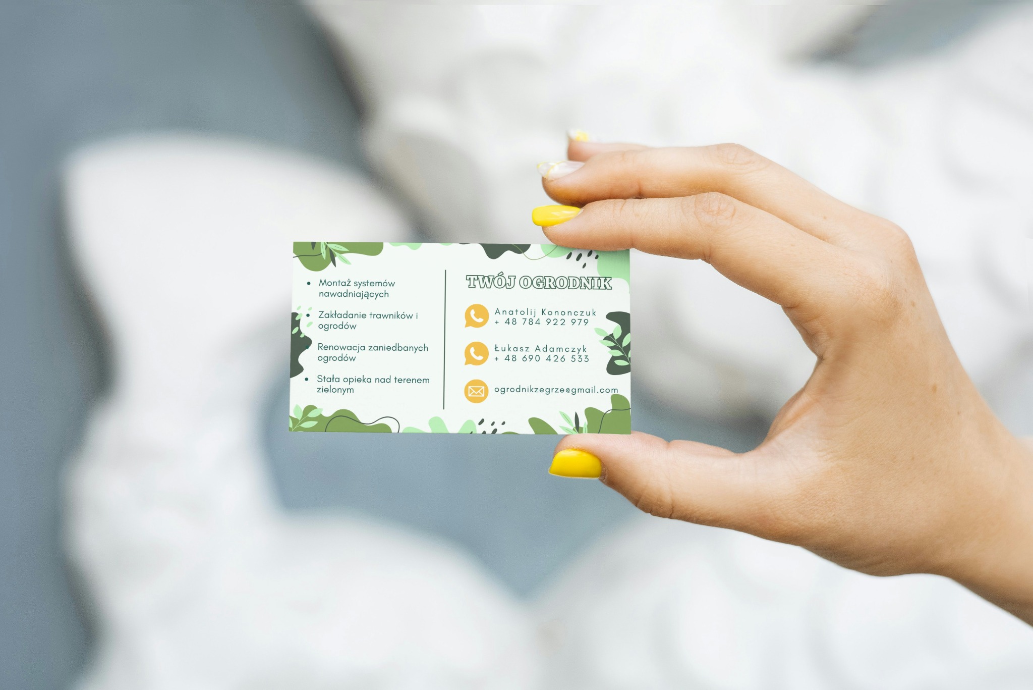 Dłoń prezentuje wizytówkę firmy ogrodniczej z zielonymi elementami graficznymi i danymi kontaktowymi, w tym adres e-mail i numery telefonów.