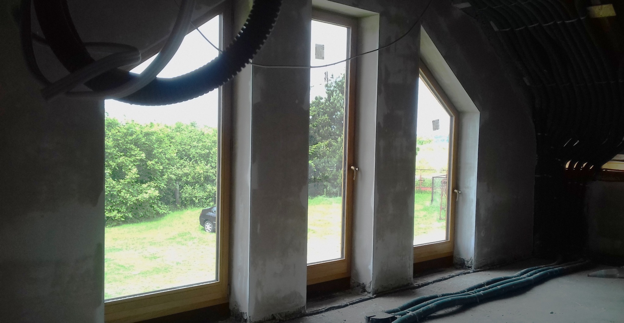 Surowe ściany po nałożeniu tynku w Katowicach, widoczne drewniane ramy okienne i wystające przewody. Prace wykończeniowe w trakcie.