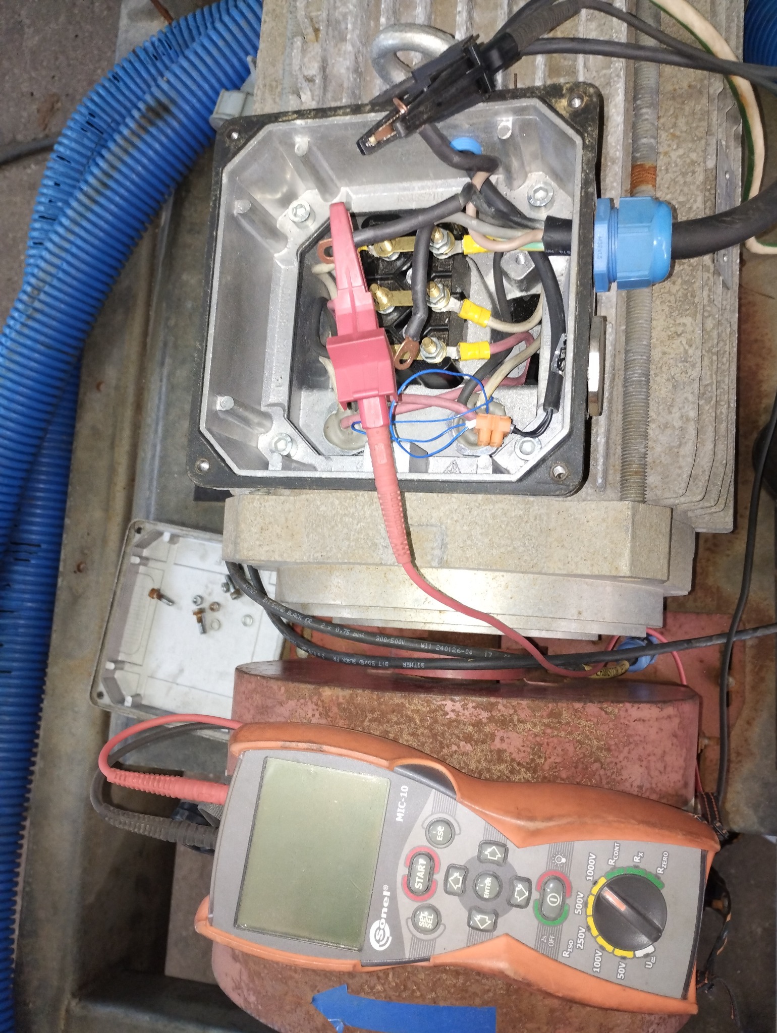 Miernik Sonel MIC-10 podłączony do skrzynki z przewodami elektrycznymi, widoczne złącza, kable i zaciski. Pomiar elektryczny w trakcie realizacji.