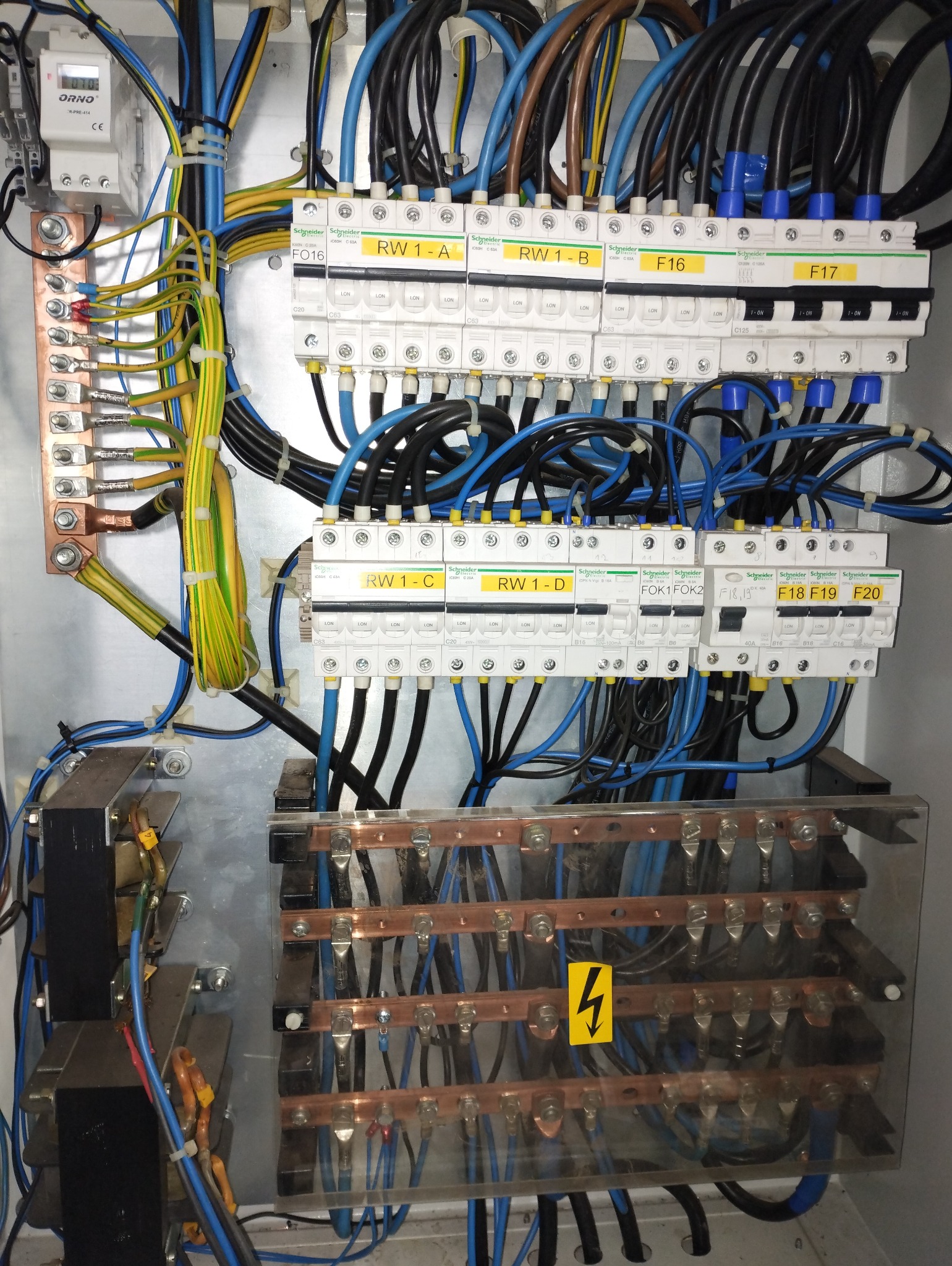 Rozdzielnia elektryczna z bezpiecznikami, przewodami i elementami zasilania. Widoczne oznaczenia na bezpiecznikach i tabliczka ostrzegawcza o wysokim napięciu.