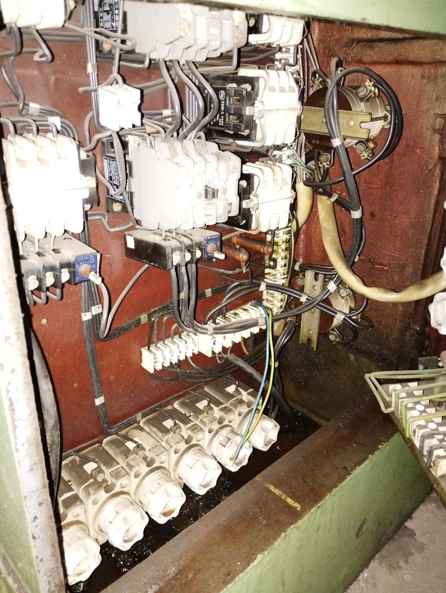 Wnętrze skrzynki elektrycznej z bezpiecznikami, przewodami i elementami sterującymi. Widoczne złącza, kable i osprzęt. Skupienie na technicznym aspekcie instalacji.