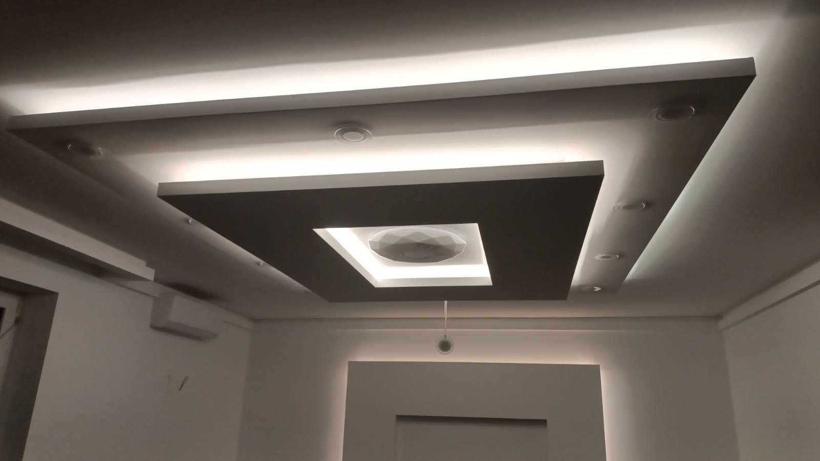 Podwieszany sufit z oświetleniem LED, kwadratowa konstrukcja z centralnym punktem świetlnym. Nowoczesny design, subtelne światło, minimalistyczne wykończenie wnętrza.