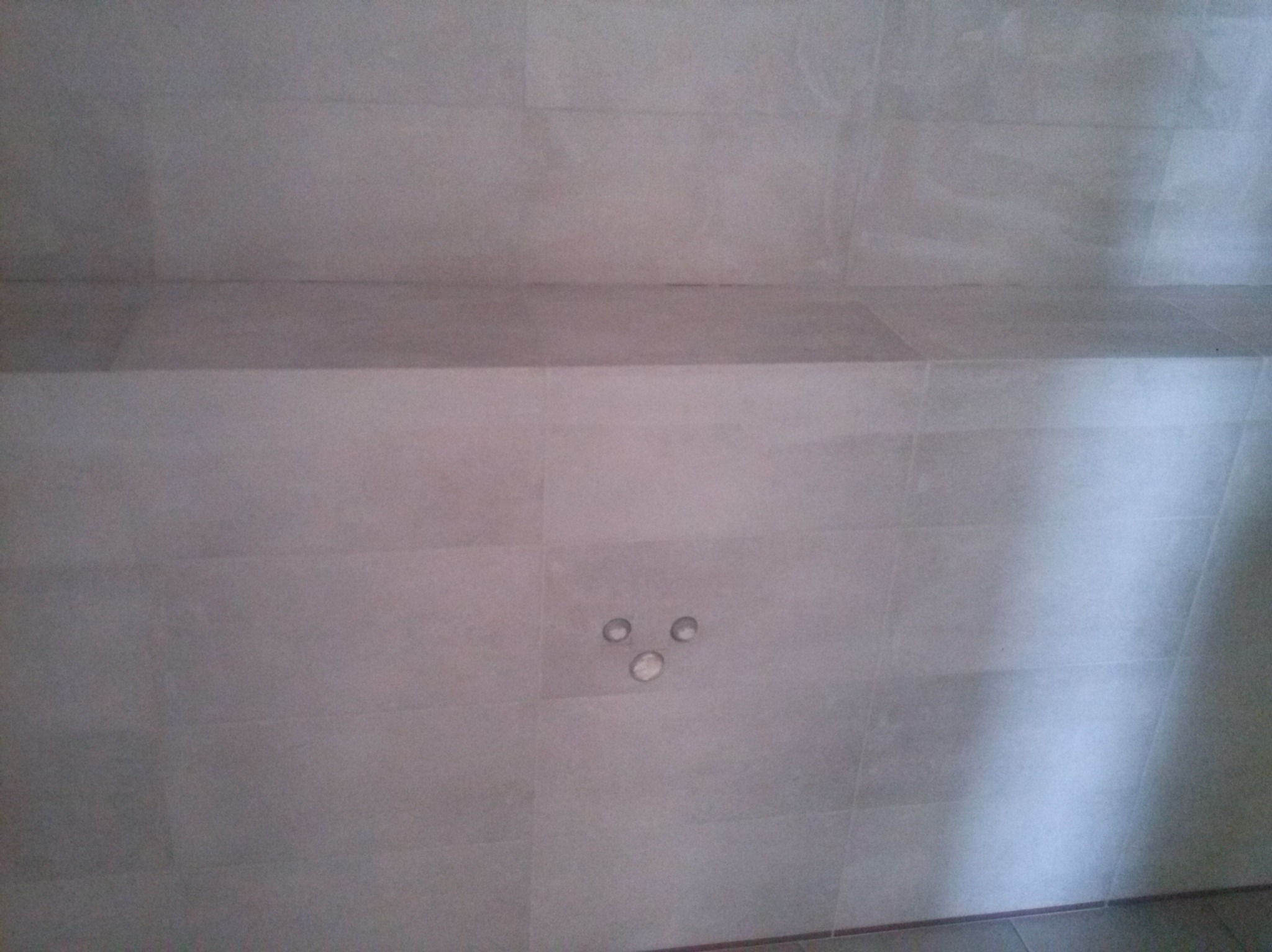 Jasnoszara ściana wyłożona płytkami z trzema okrągłymi otworami na oświetlenie punktowe. Minimalistyczny design, neutralna kolorystyka.