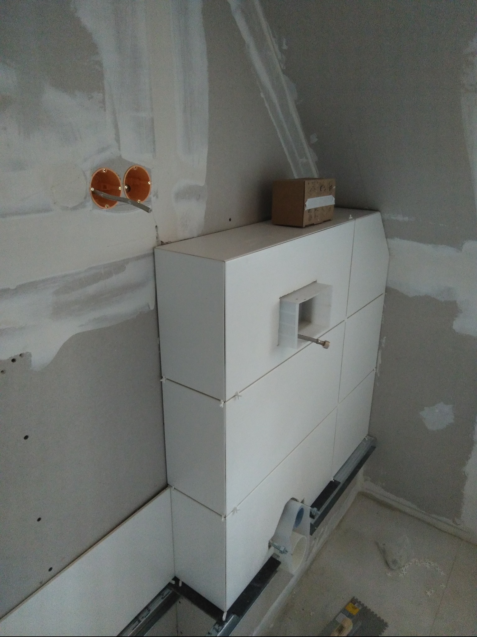 Białe płytki ułożone na stelażu podtynkowym w łazience w trakcie remontu. Widoczne elementy instalacji i narzędzia glazurnicze. Ściany przygotowane pod dalsze prace wykończeniowe.