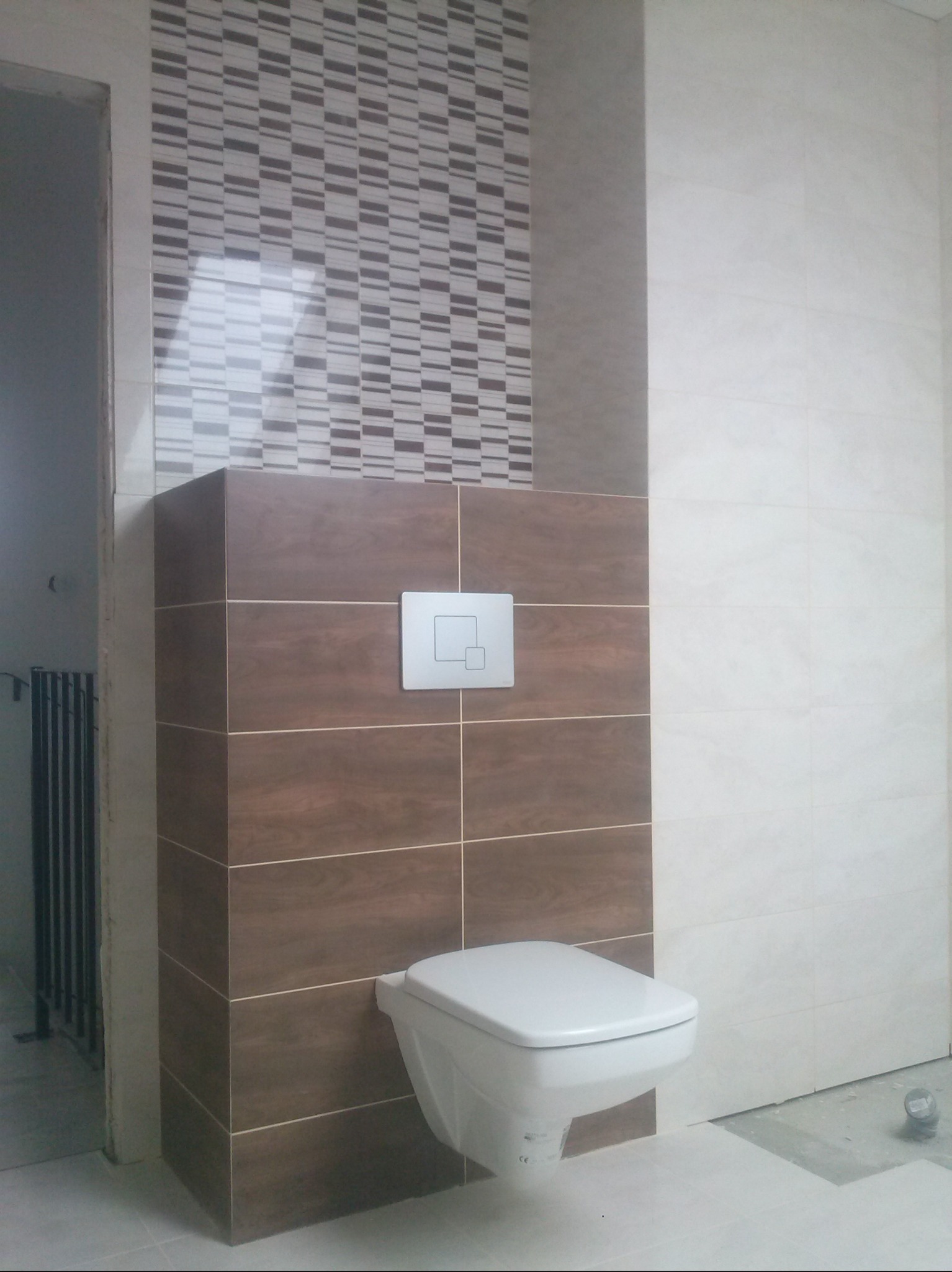 Wykończona toaleta podwieszana z brązowymi płytkami i mozaiką w Jastrzębiu. Widoczny przycisk spłukiwania i fragment grzejnika za ścianą.