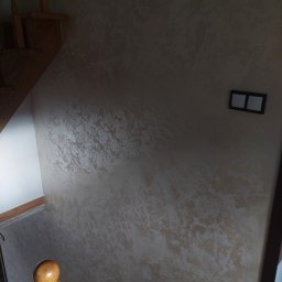 USŁUGI REMONTOWO-BUDOWLANE PIOTR JANOWSKI - Dekoracyjna ściana w Dubiecku z efektem marmuru, widoczna przy schodach. Subtelne oświetlenie podkreśla unikalną fakturę. Obok włącznik światła.