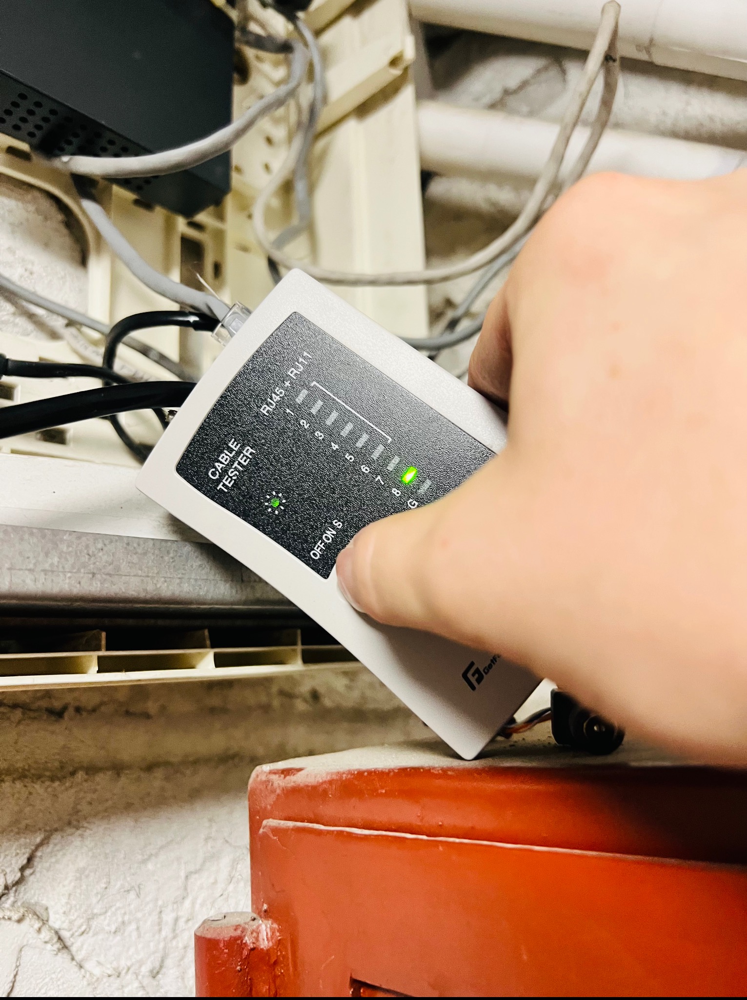 Testowanie kabla sieciowego testerem. Widoczne kable, listwa i tester z zapaloną diodą. Kontrola połączeń w instalacji.