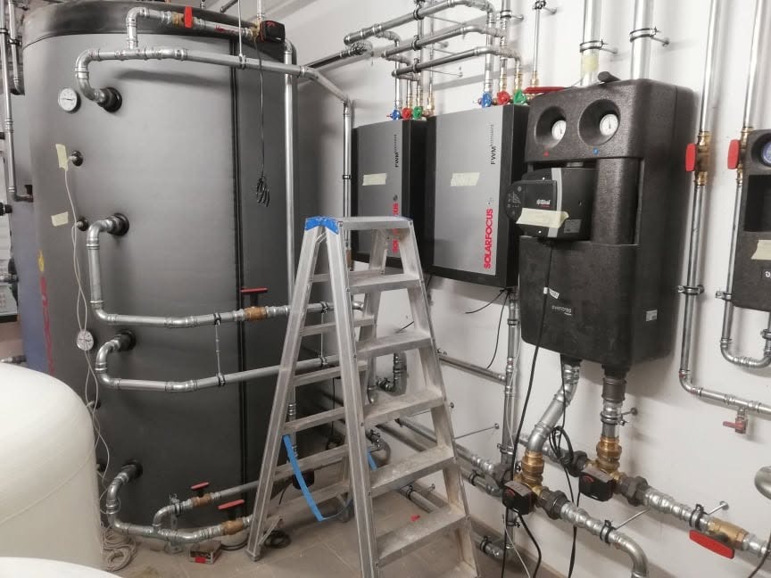 Instalacja pieca gazowego i zbiornika w Gostyniu. Widoczne rury, zawory i drabina. Elementy systemu grzewczego. Szare zbiorniki i czarne moduły.