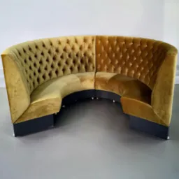 Półokrągła sofa modułowa z welurową tapicerką w odcieniach złota i brązu, z pikowaniem typu chesterfield, na ciemnych, niskich nóżkach.