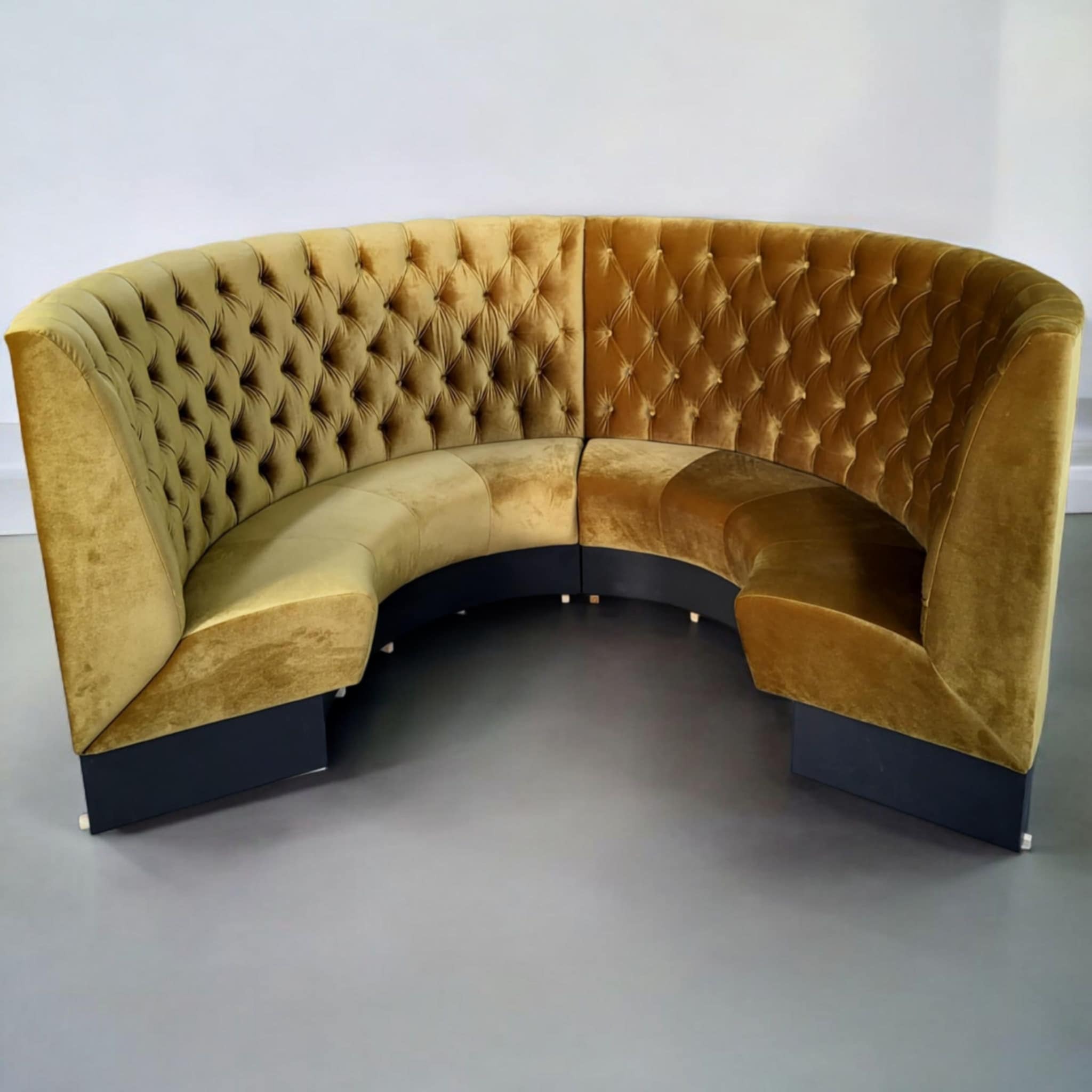 Półokrągła sofa modułowa z welurową tapicerką w odcieniach złota i brązu, z pikowaniem typu chesterfield, na ciemnych, niskich nóżkach.