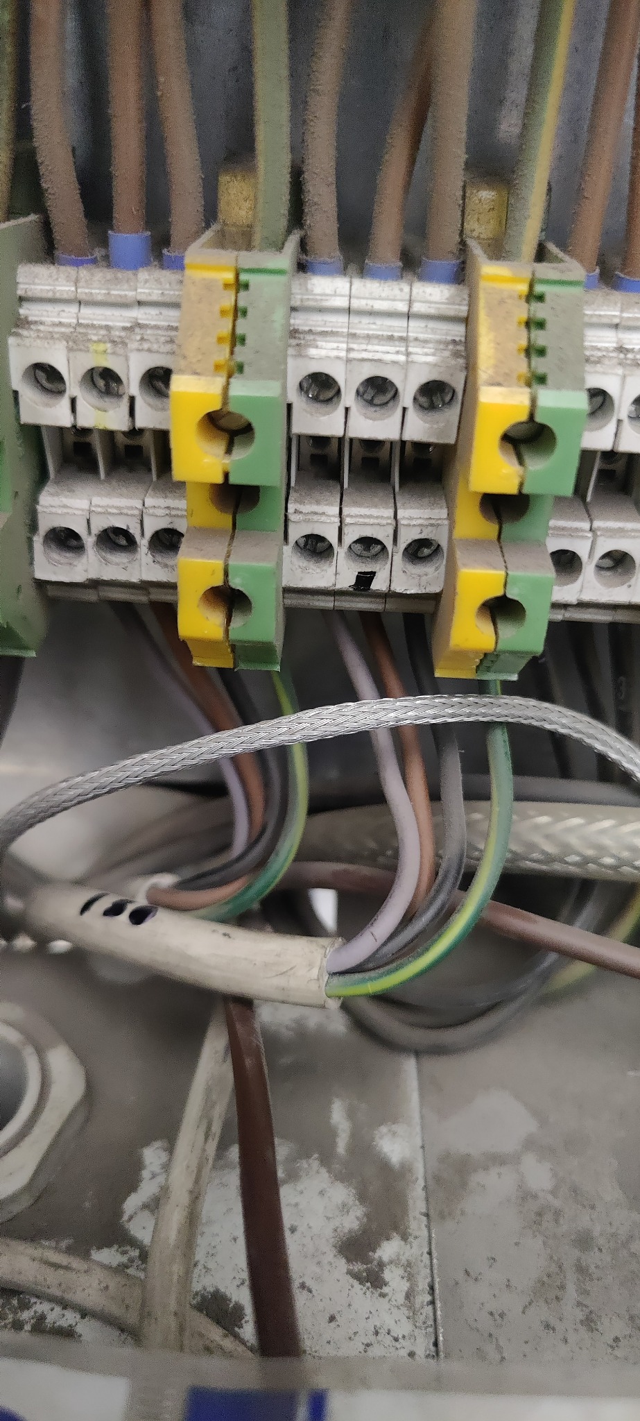 Szczegółowe ujęcie podłączenia kabli do listwy zaciskowej z elementami w kolorze żółto-zielonym. Widoczne przewody w izolacji o różnych kolorach.