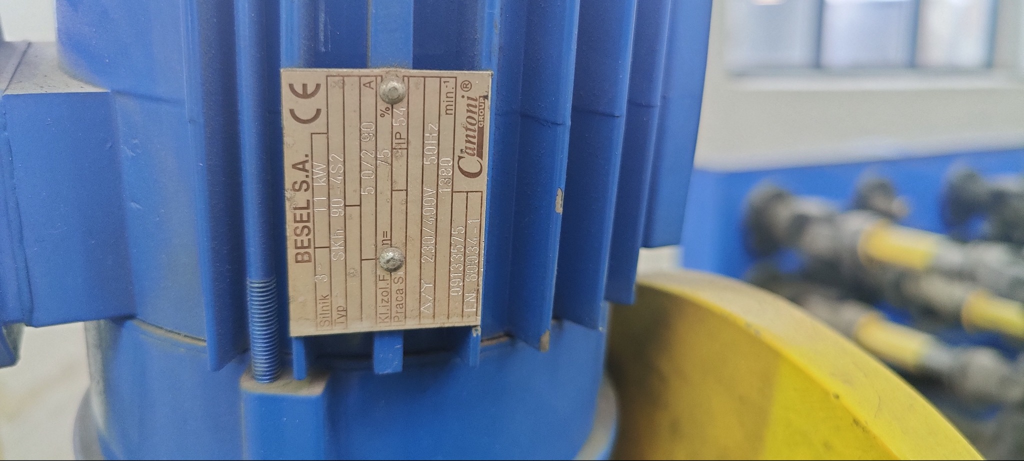 Tabliczka znamionowa silnika elektrycznego Besel S.A. z danymi technicznymi, umieszczona na niebieskiej obudowie silnika. Widoczne śruby mocujące tabliczkę.