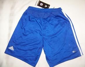 Niebieskie sportowe spodenki Adidas z białymi paskami po bokach, widoczne logo marki w lewym dolnym rogu oraz metka z logo klubu sportowego w górnej części.