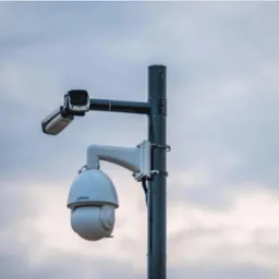 Dwie kamery monitoringu Dahua na słupie z widocznymi przewodami, na tle pochmurnego nieba. Górna kamera w obudowie prostokątnej, dolna PTZ w obudowie kopułkowej.