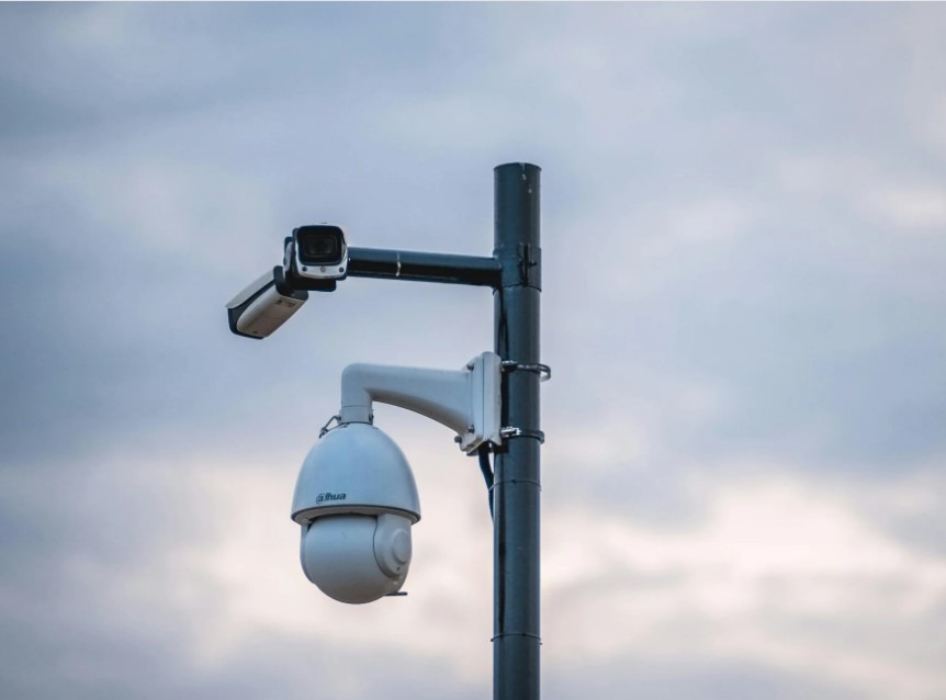 Dwie kamery monitoringu Dahua na słupie z widocznymi przewodami, na tle pochmurnego nieba. Górna kamera w obudowie prostokątnej, dolna PTZ w obudowie kopułkowej.