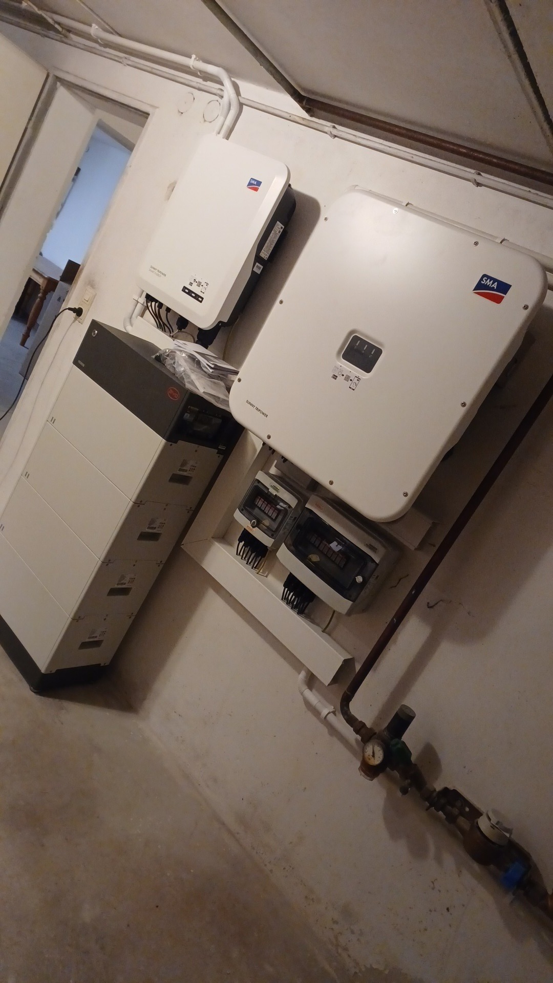 Instalacja magazynu energii: biała bateria BYD, inwertery SMA, rozdzielnica elektryczna na ścianie w piwnicy. Widoczne rury instalacyjne.