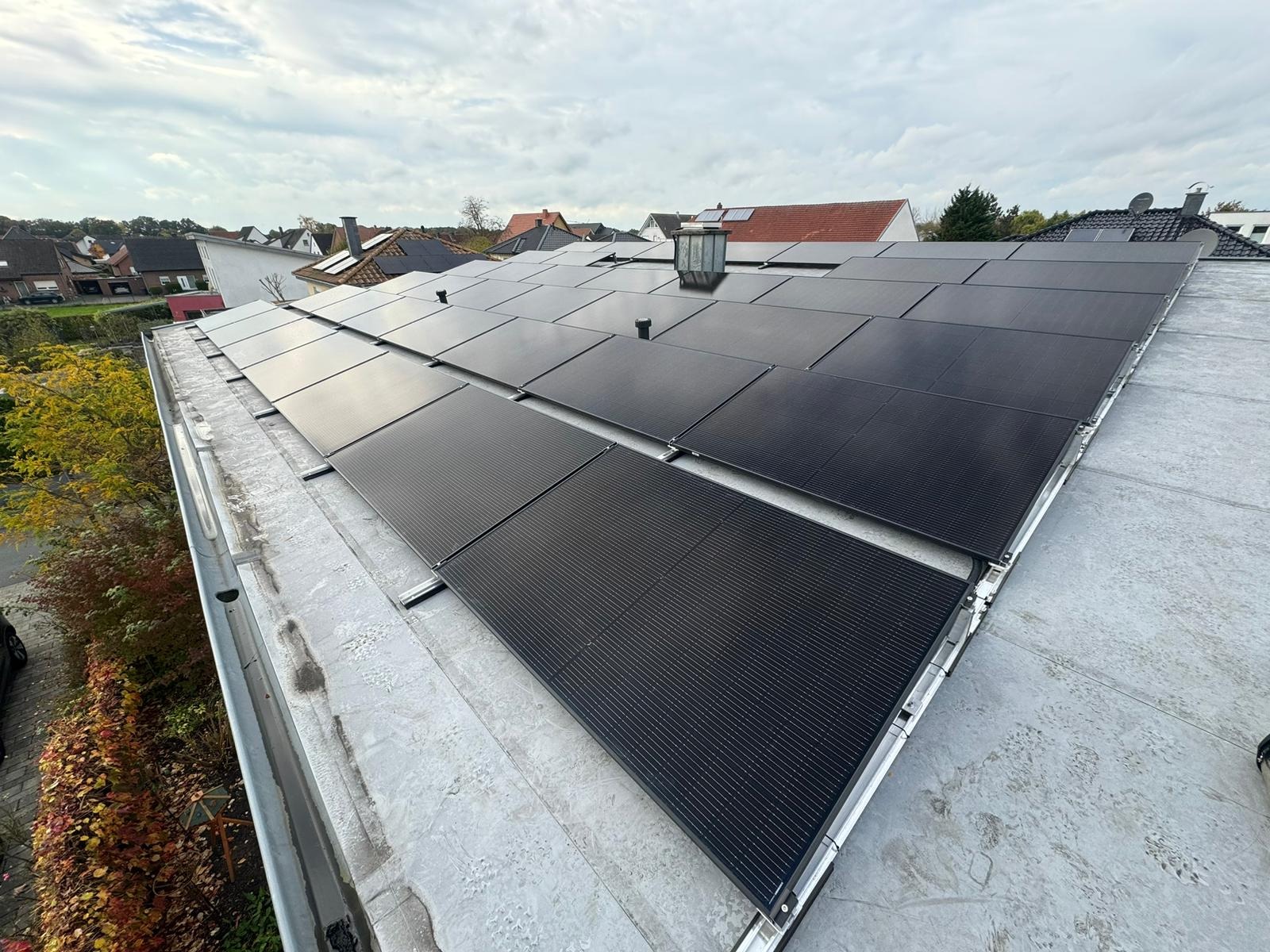 Panele fotowoltaiczne zamontowane na płaskim dachu budynku mieszkalnego, widok z góry, pochmurne niebo w tle.