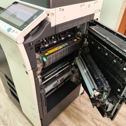 R-TECH ŁUKASZ ROSOWSKI - Otwarta kserokopiarka A3 z widocznymi elementami wewnętrznymi, takimi jak moduł bębna i podajnik papieru, sugerująca serwis lub naprawę. Widoczne ostrzeżenia.