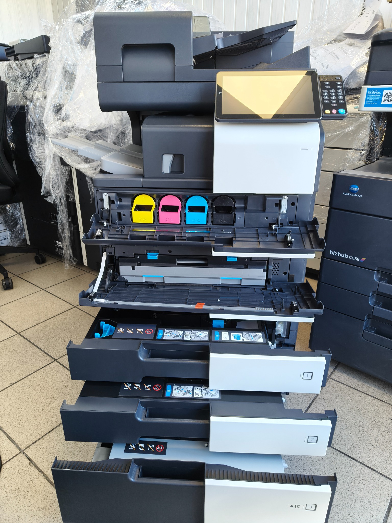 Wielofunkcyjna kserokopiarka Konica Minolta Bizhub C558 z otwartymi podajnikami papieru i pojemnikami na tusze w Płocku, gotowa do serwisu.