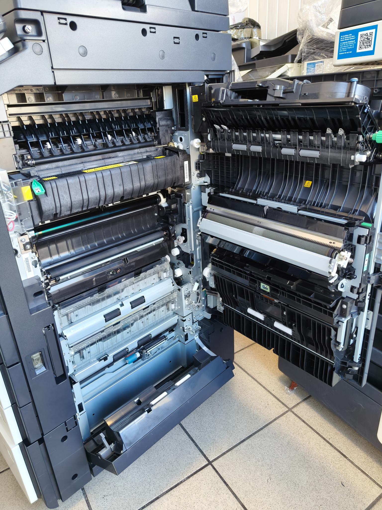 Otwarta kserokopiarka A3 ukazująca wewnętrzne mechanizmy, rolki i podajniki papieru; widoczne elementy konstrukcyjne i ostrzeżenia na obudowie.