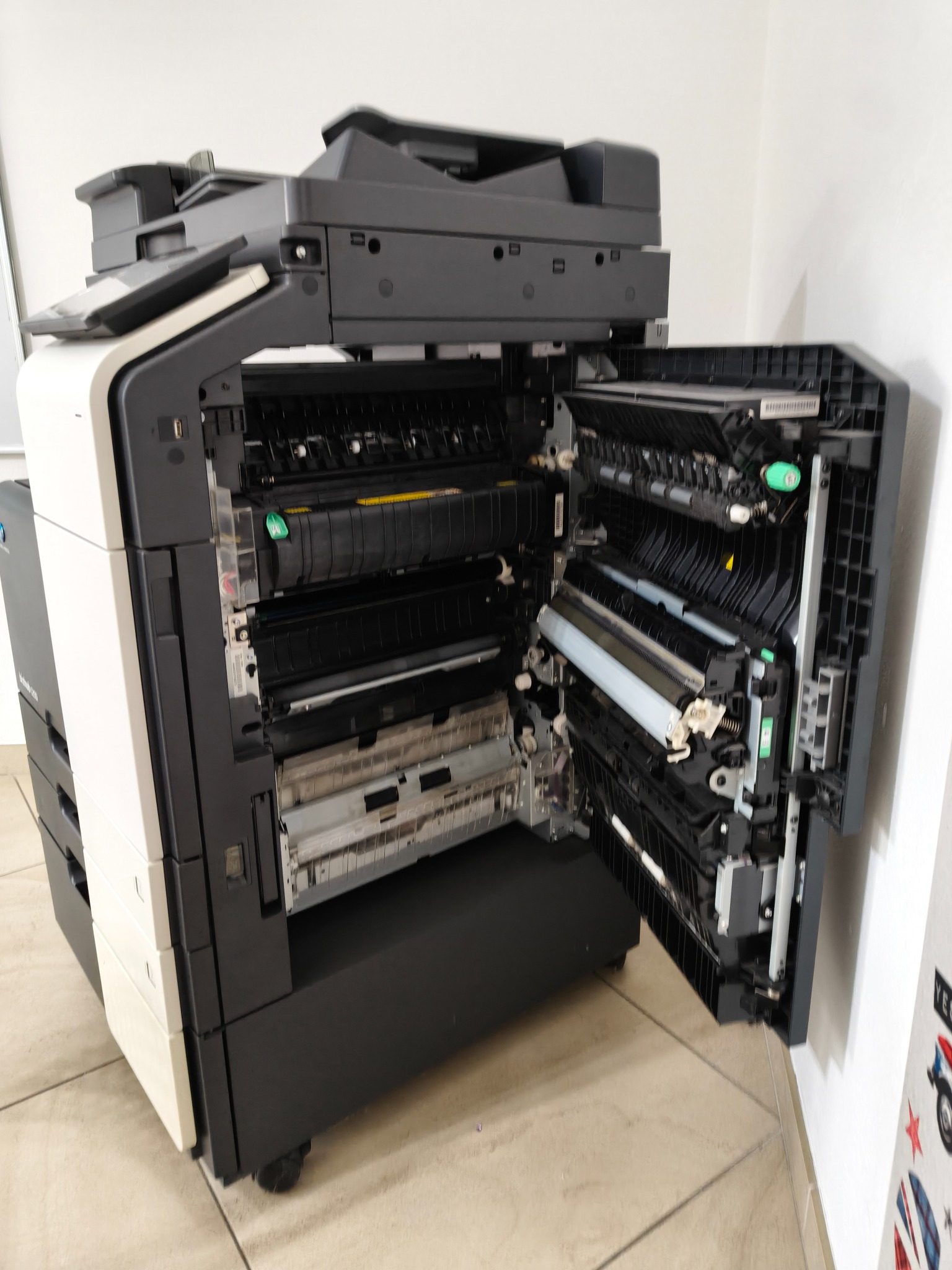 Otwarta kserokopiarka wielkoformatowa A3/A0, ukazująca wewnętrzne mechanizmy. Widoczne rolki, podajniki papieru i elementy elektroniki. Sprzęt biurowy w trakcie serwisu.