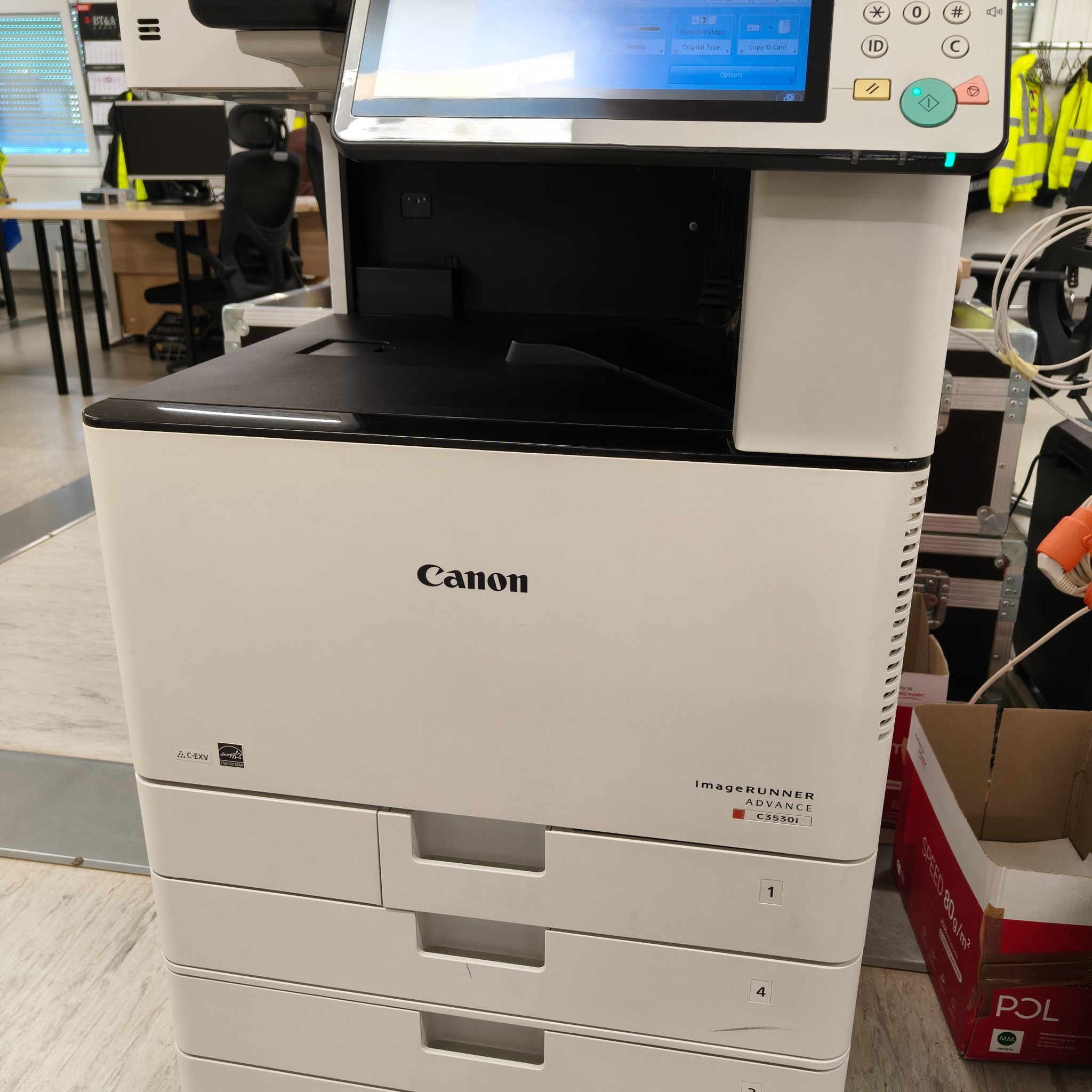 Kserokopiarka Canon imageRUNNER ADVANCE C3530i z panelem dotykowym w biurze. Widoczne oznaczenia szuflad na papier i logo Energy Star. Obok karton z papierem.
