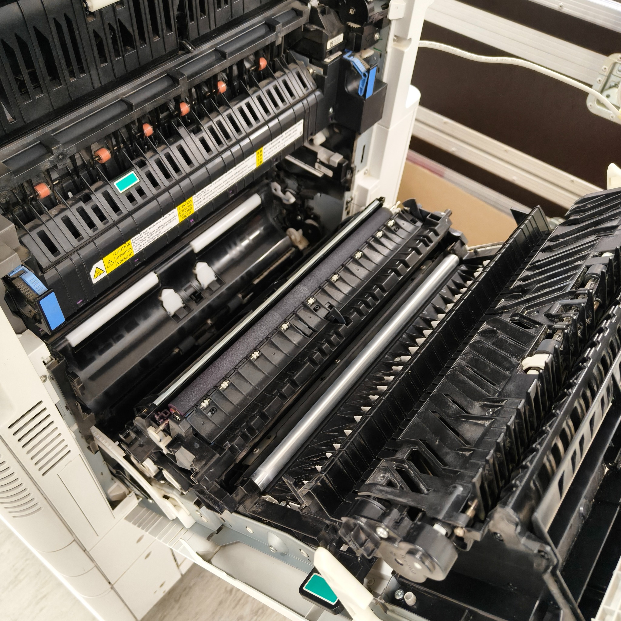 Otwarta kserokopiarka A3 z widocznymi wewnętrznymi mechanizmami, w tym rolkami i elementami podajnika papieru. Widoczne ostrzeżenia dotyczące gorących elementów.