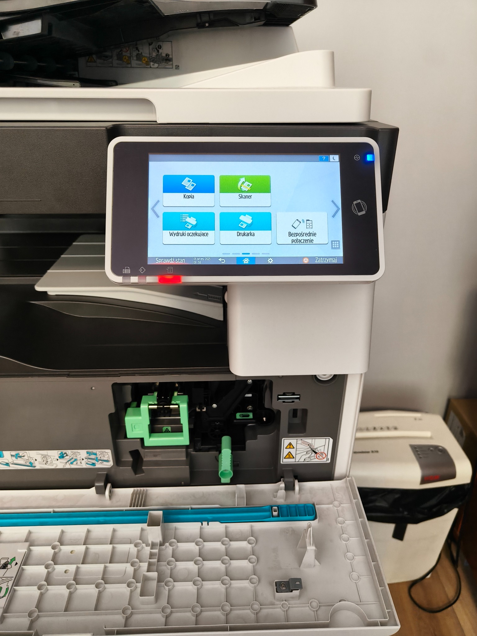 Otwarta kserokopiarka wielkoformatowa z panelem dotykowym wskazującym opcje kopiowania, skanowania i drukowania. Widoczny mechanizm wewnętrzny urządzenia.