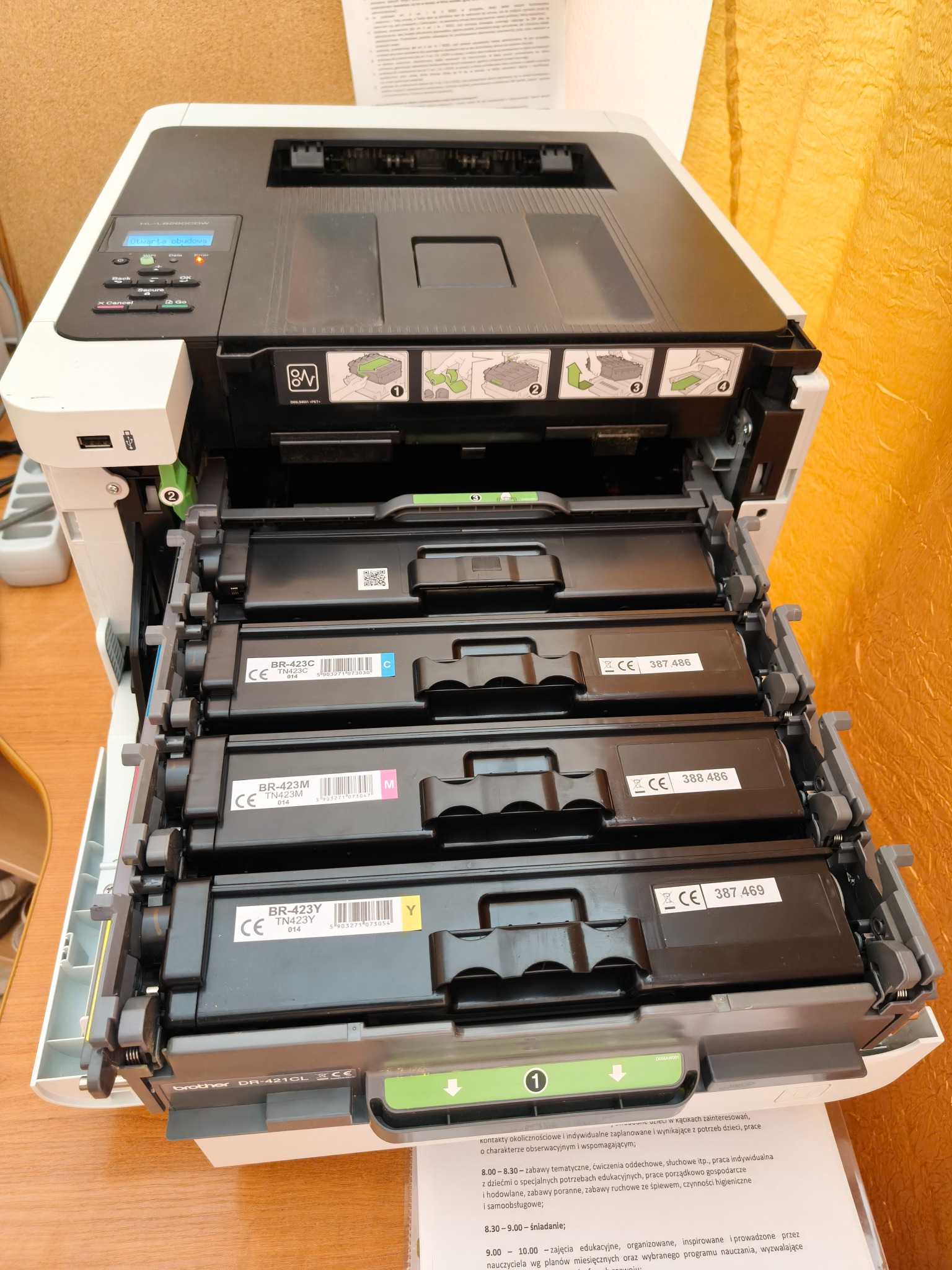 Otwarta kserokopiarka Brother z wysuniętymi czterema pojemnikami na tonery: czarnym, żółtym, magenta i cyjan. Widoczne etykiety z oznaczeniami kolorów i numerami seryjnymi.
