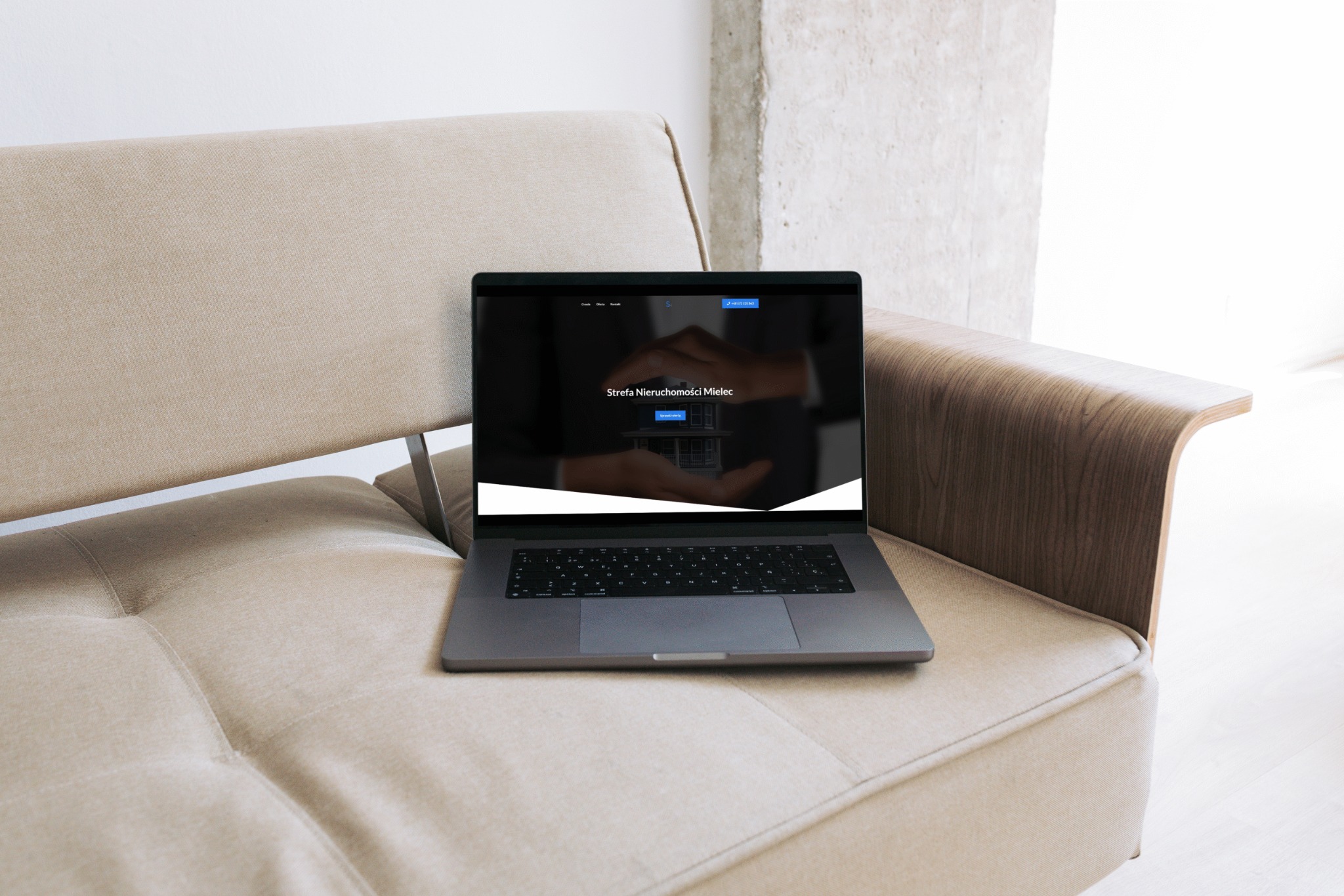 Laptop na sofie prezentuje stronę www 'Strefa Nieruchomości Mielec'. Minimalistyczny design, stonowana kolorystyka. Widok z bliska, naturalne światło.