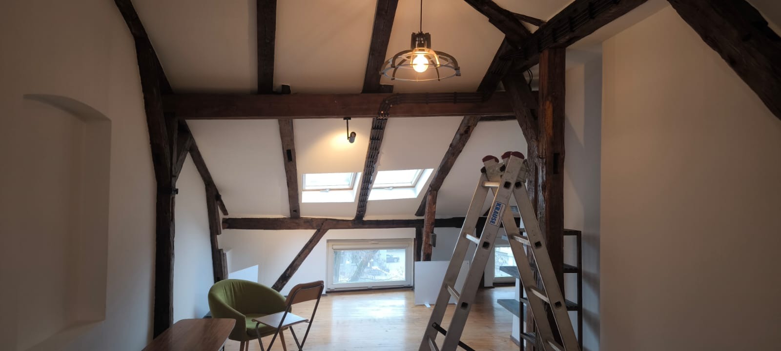 Poddasze po remoncie: białe ściany, drewniane belki stropowe, skosy, okna dachowe, drabina Krause. Widok na odnowione wnętrze.