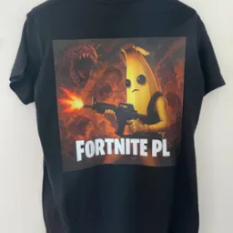 Czarna koszulka z nadrukiem postaci z gry Fortnite PL, wisząca na wieszaku na tle białej ściany. Grafika w tonacji pomarańczowo-brązowej.