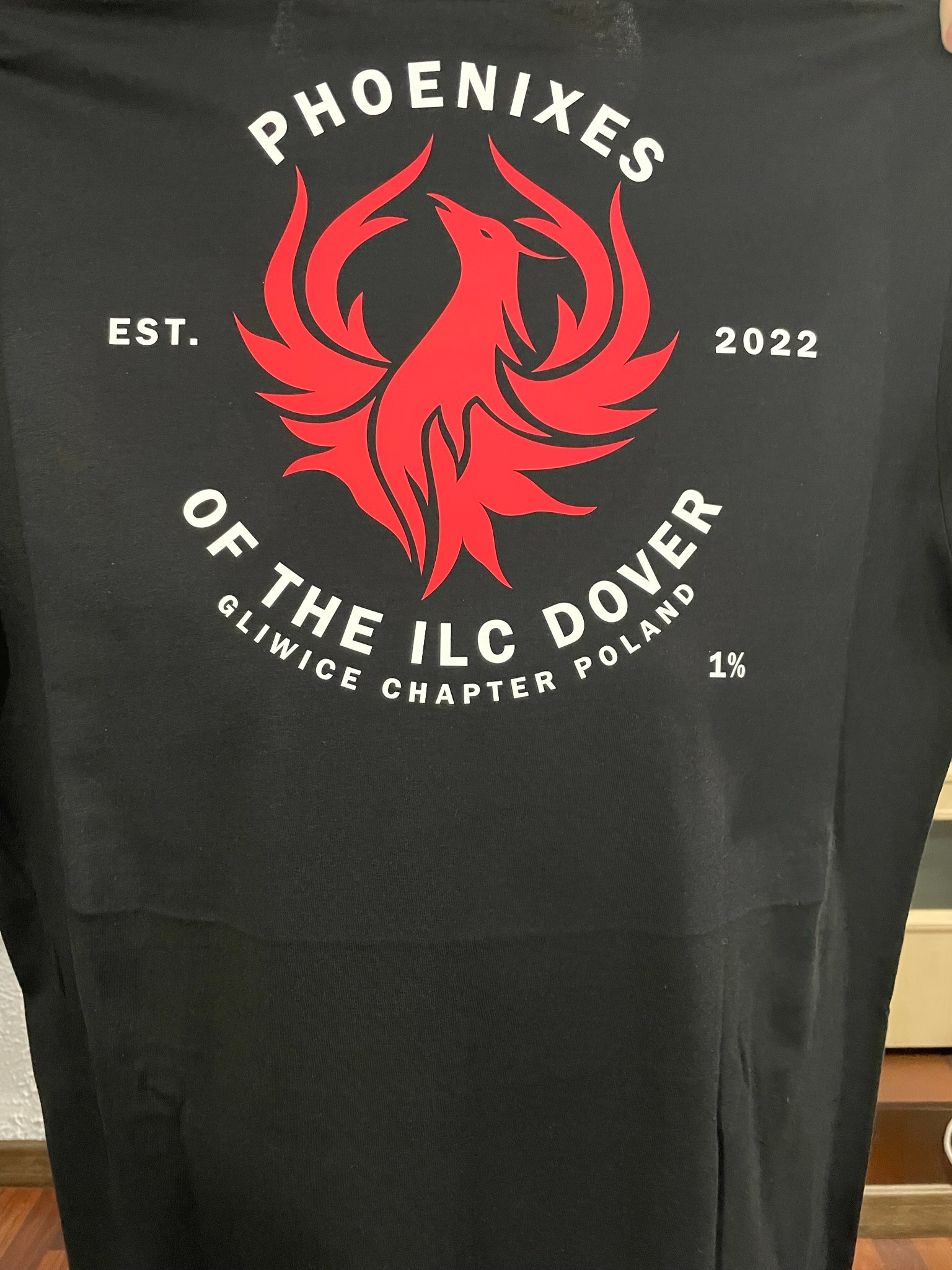 Czarna koszulka z czerwonym nadrukiem logo Phoenixes, EST. 2022, OF THE ILC DOVER, Gliwice Chapter Poland, 1%. Widoczne detale nadruku i materiału.