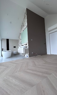 Nowoczesna łazienka z podłogą w jodełkę, marmurową ścianą i minimalistyczną armaturą. Widoczne dwie umywalki i wolnostojąca wanna.