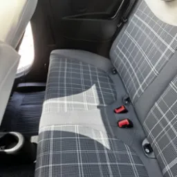 Wnętrze samochodu: tylna kanapa z szaro-białą tapicerką w kratę, widoczne pasy bezpieczeństwa i gumowe dywaniki. Czyste i zadbane.
