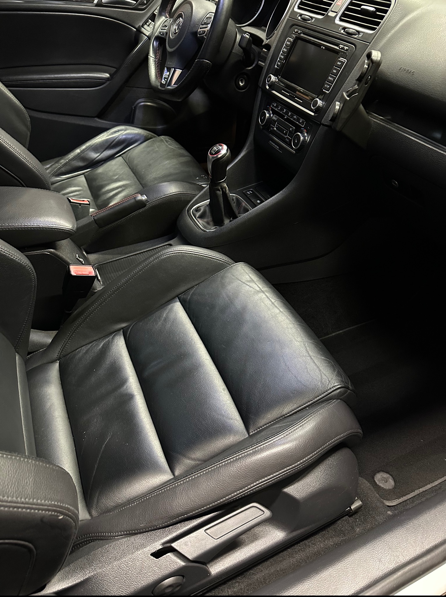 Wnętrze czarnego samochodu, widoczne skórzane fotele z wyraźnymi śladami użytkowania, deska rozdzielcza i kierownica.