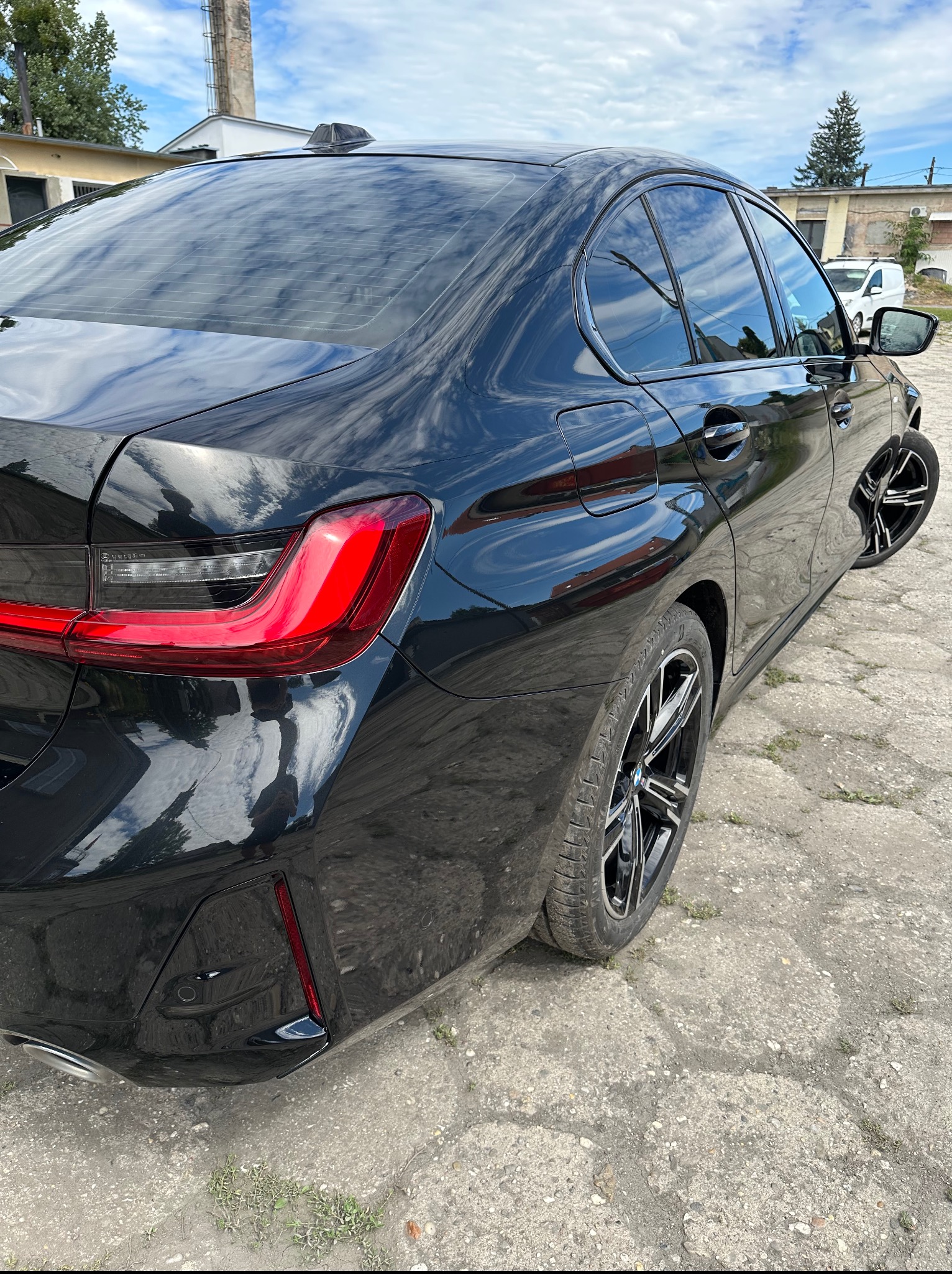 Błyszczący, czarny samochód po usłudze mycia w Kędzierzynie-Koźlu. Widok z tyłu, z wyraźnym odbiciem nieba w lakierze. Felgi aluminiowe.