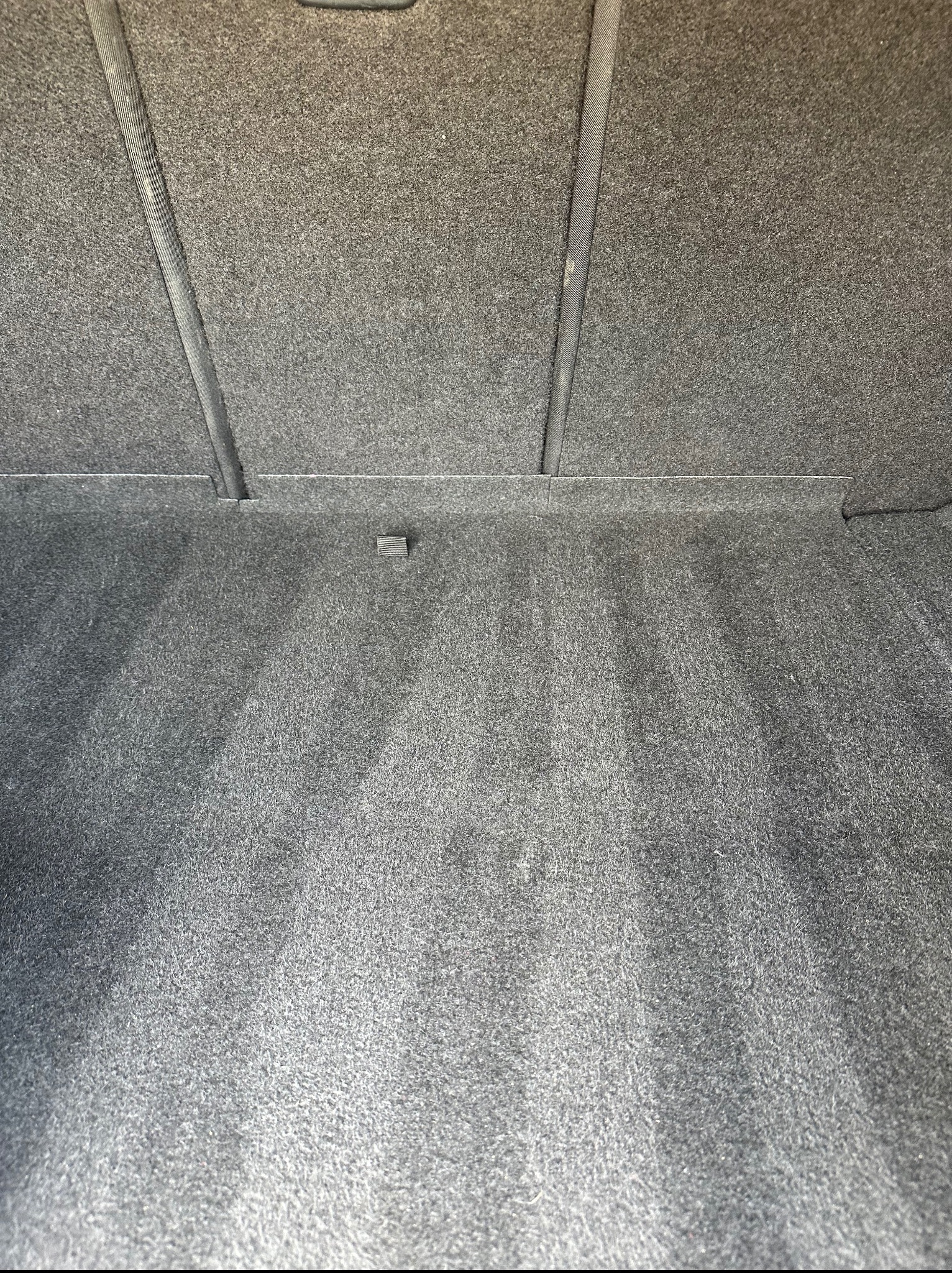 Szara, tekstylna tapicerka bagażnika samochodowego po czyszczeniu, widoczne jaśniejsze ślady po praniu.