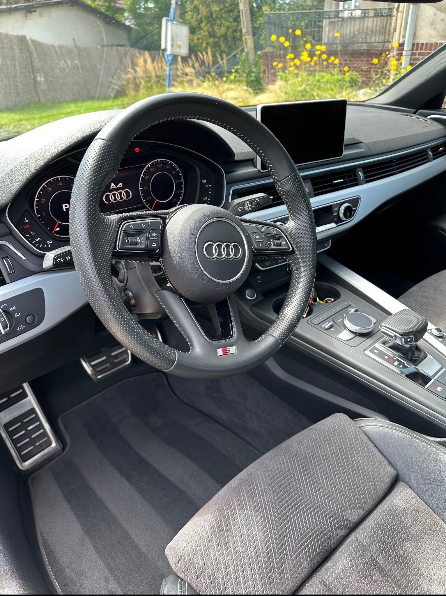 Wnętrze Audi A4 po detailingu: czysta kierownica z perforowanej skóry, deska rozdzielcza z ekranem, odświeżone dywaniki i fotele z wyraźnym wzorem. Widok z perspektywy pasażera.