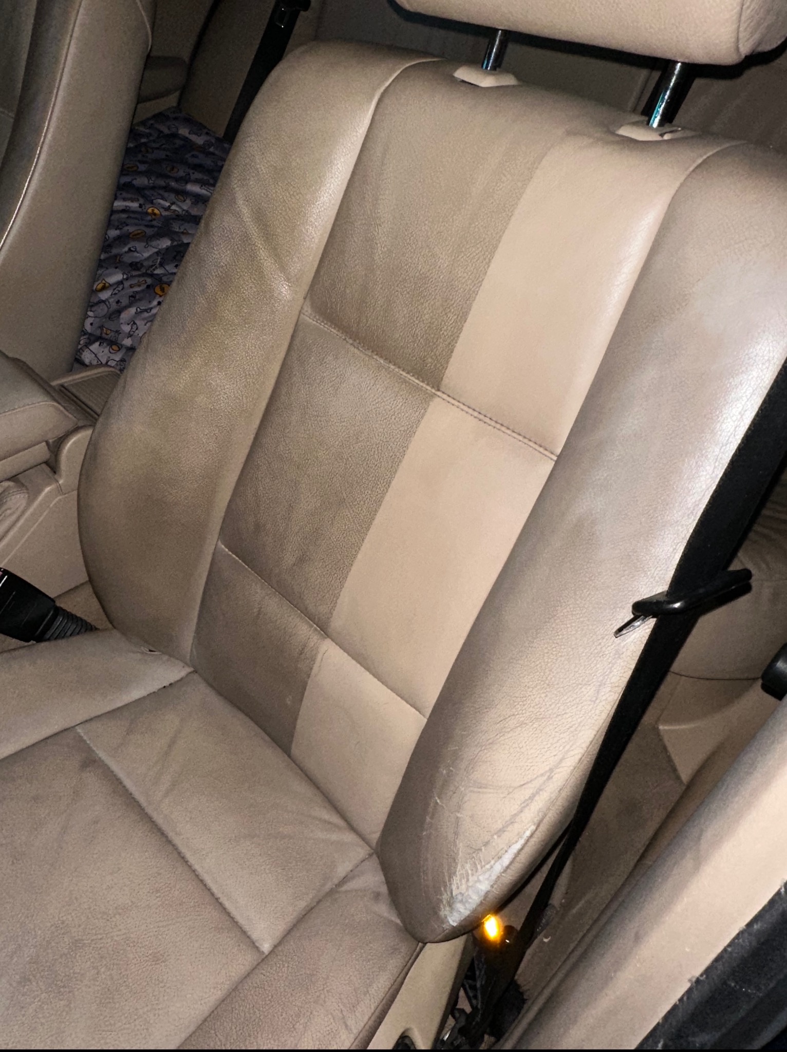 Beżowy, skórzany fotel samochodowy, widoczny w połowie wyczyszczony, z wyraźną różnicą w odcieniu i czystości między obszarami przed i po czyszczeniu tapicerki.