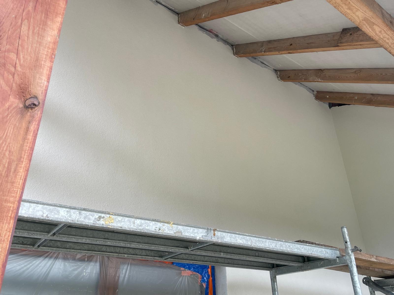 Świeżo pomalowana, jasna ściana wewnętrzna z widocznym rusztowaniem i drewnianymi elementami konstrukcyjnymi stropu. Ujęcie z dołu, podkreślające wysokość pomieszczenia.