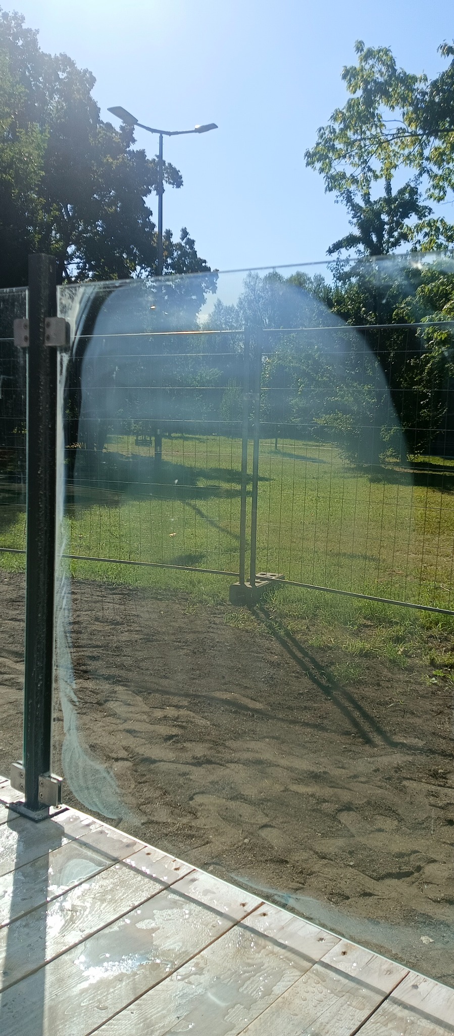 Mokre, umyte szkło balustrady balkonu z widokiem na park w słoneczny dzień. Ślady wody na drewnianej podłodze balkonu.