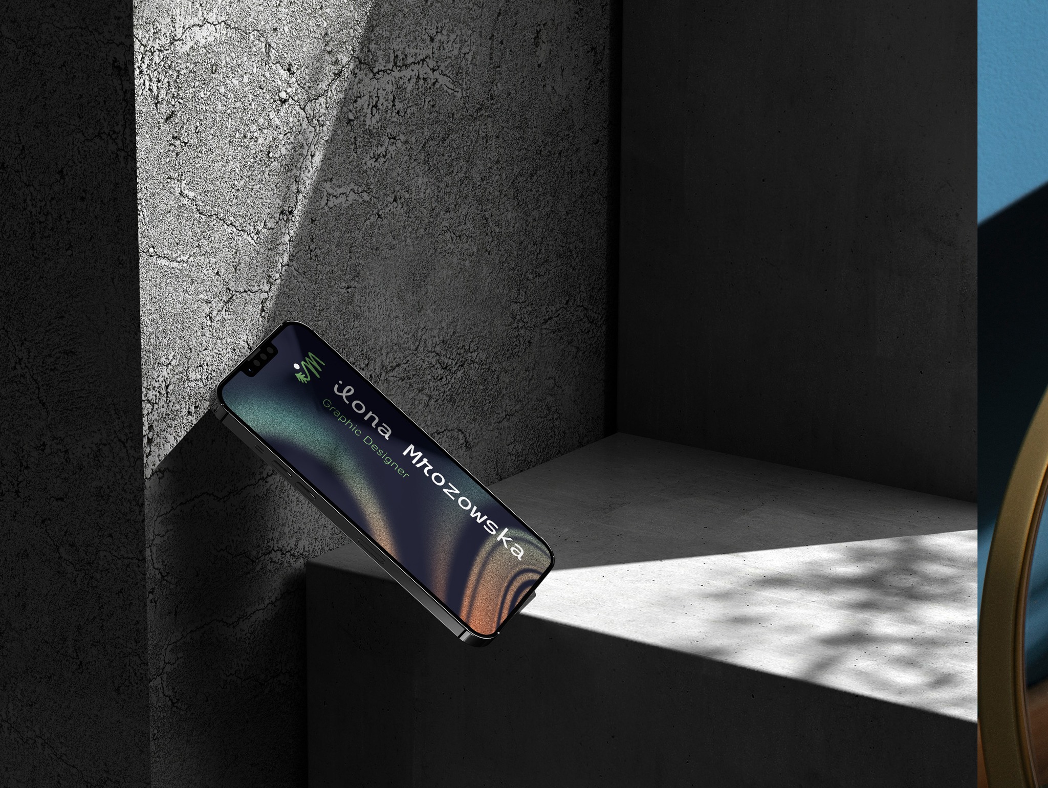 Telefon z wizytówką graficzki Ilony Mrozowskiej na tle surowego betonu w minimalistycznej aranżacji. Ciemne tło, gra światła i cienia, nowoczesny design.