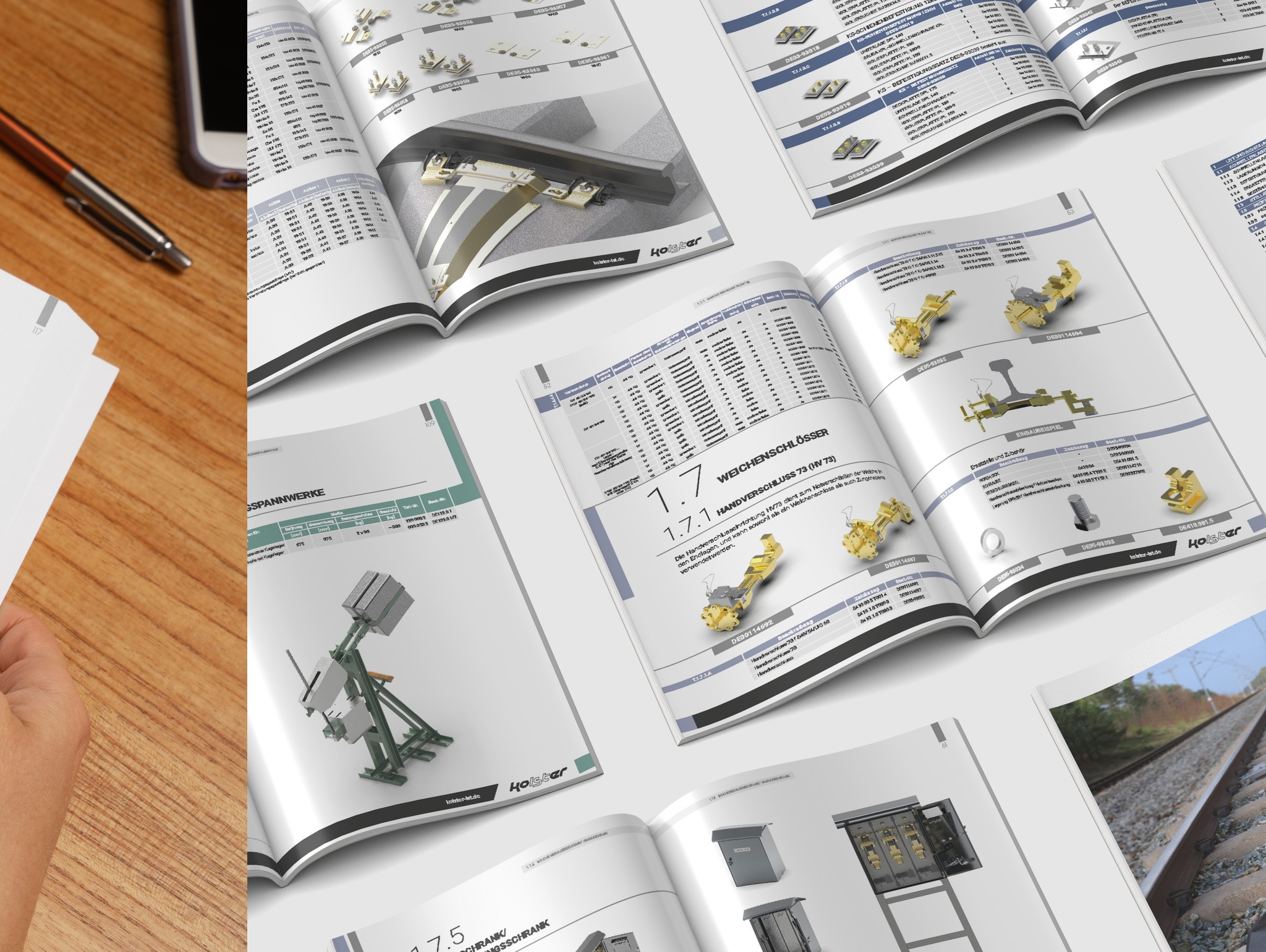 Otwarty katalog z ilustracjami technicznymi i danymi produktów firmy Kolster, widoczny na drewnianym biurku obok telefonu i długopisu. Prezentacja oferty.