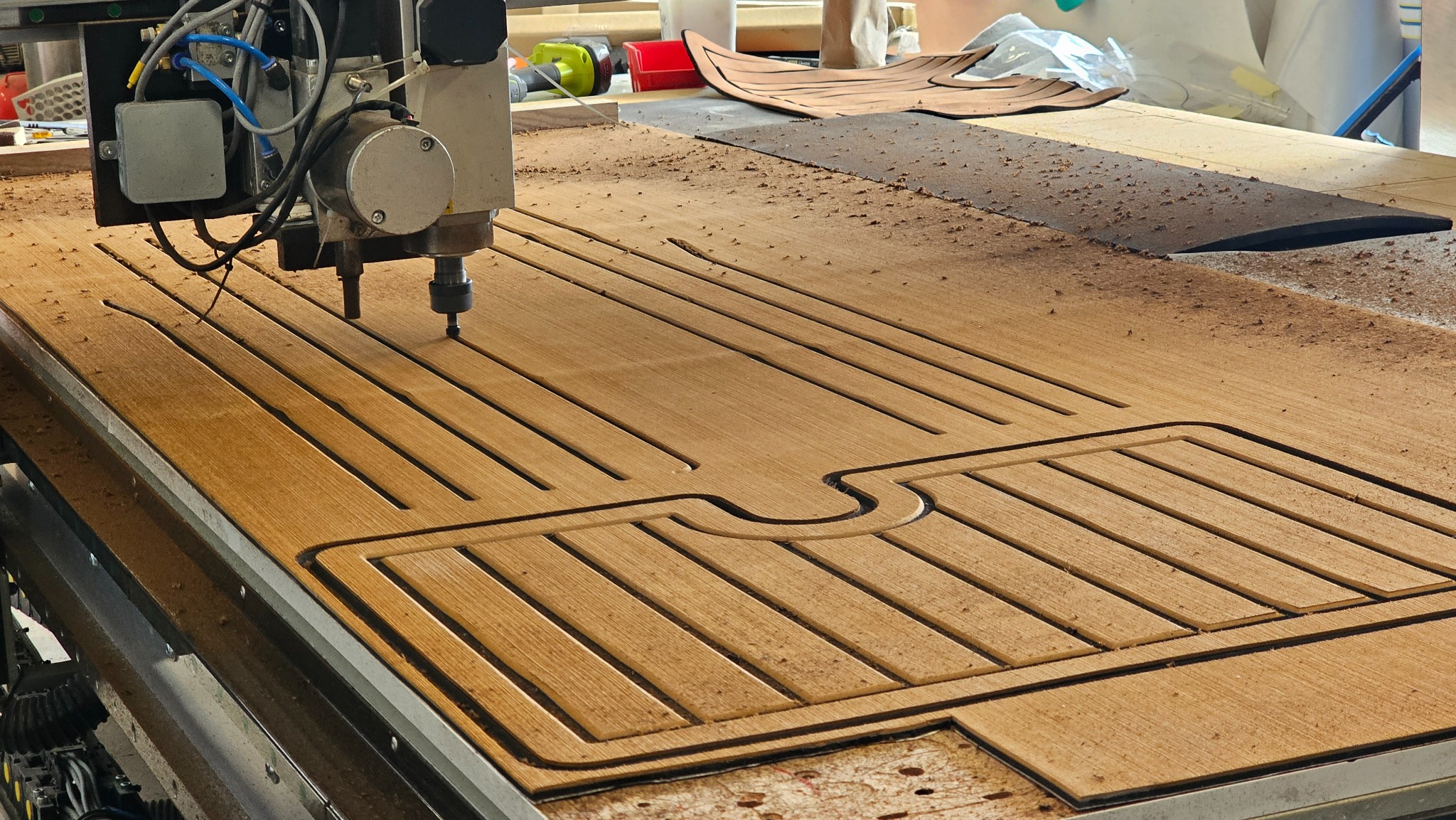 Frezarka CNC w trakcie wycinania wzoru w drewnianej płycie, widoczne wióry i fragment gotowego elementu. Detal obróbki drewna, precyzyjne wycinanie.