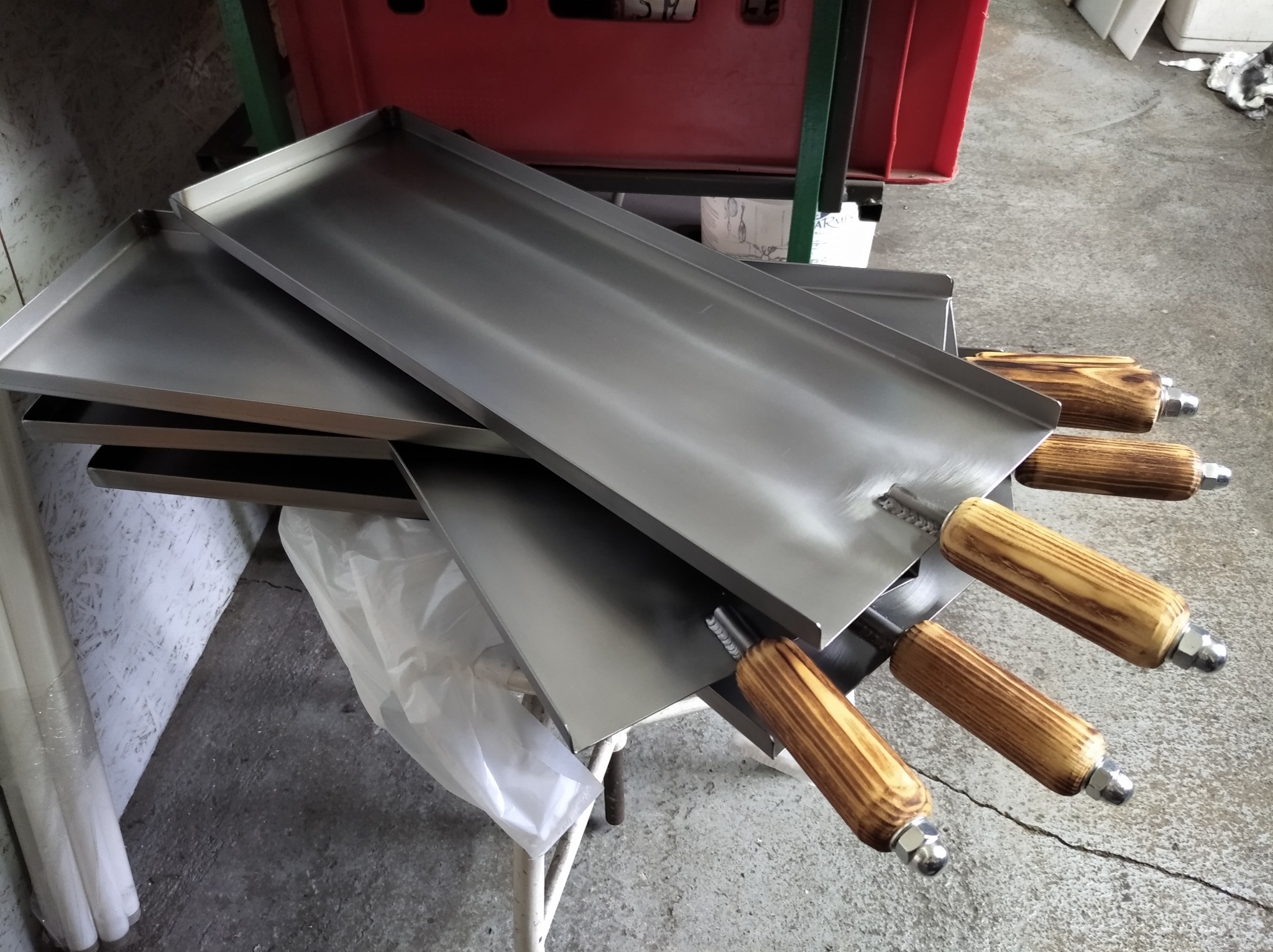 Metalowe płyty z drewnianymi uchwytami, ułożone warstwowo na stole, ukazujące precyzyjne spawy i gładkie wykończenie.