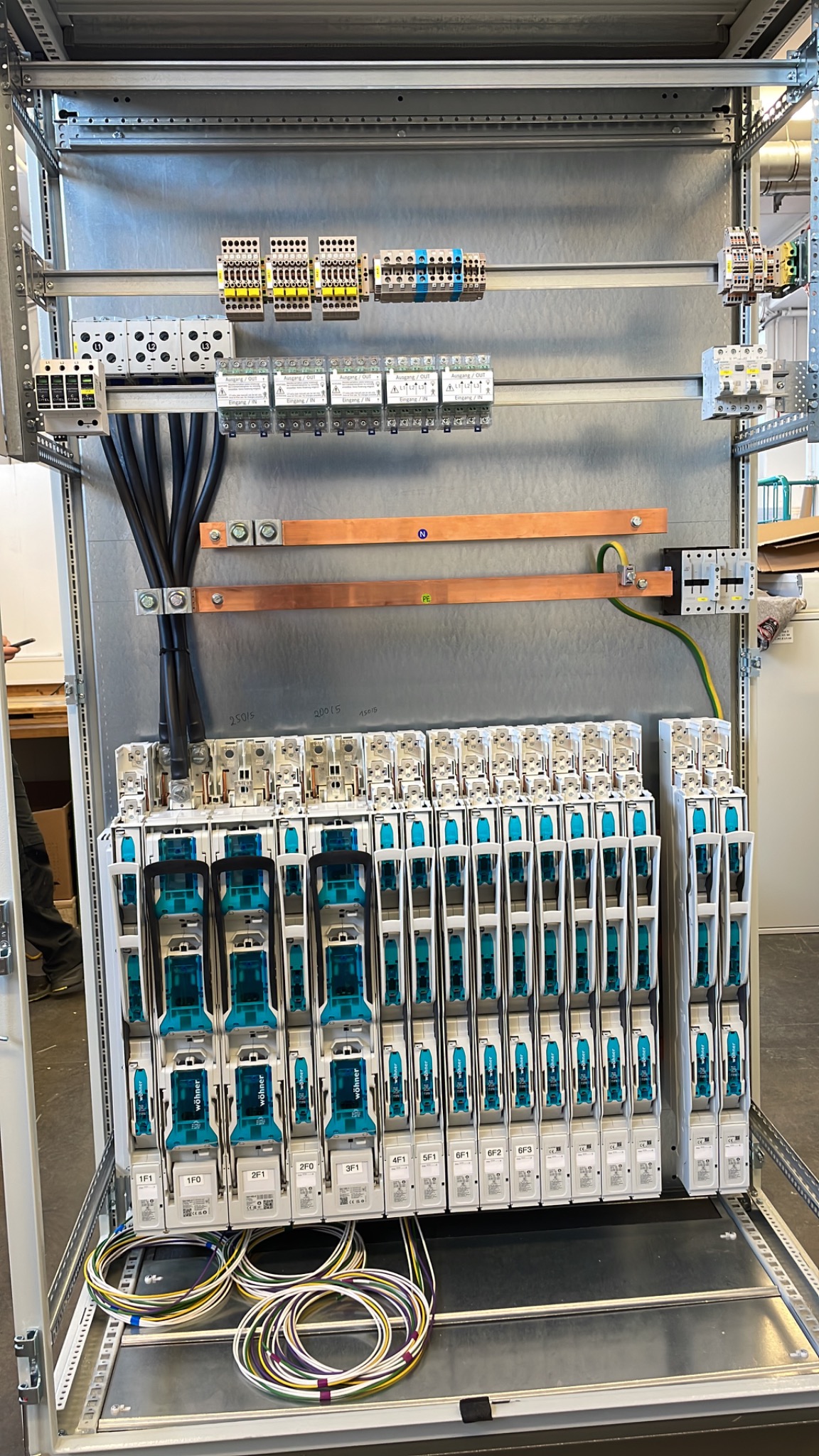 Rozdzielnica elektryczna z modułowymi zabezpieczeniami, miedzianymi szynami i podłączonymi przewodami. Widoczne oznaczenia na elementach. Instalacja wewnątrz metalowej szafy.