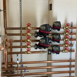 Hydro-Plumbing Ltd - Miedziana instalacja grzewcza z zaworami i pompami obiegowymi Grundfos, zamontowana na ścianie. Widoczne elementy mocujące i manometry.