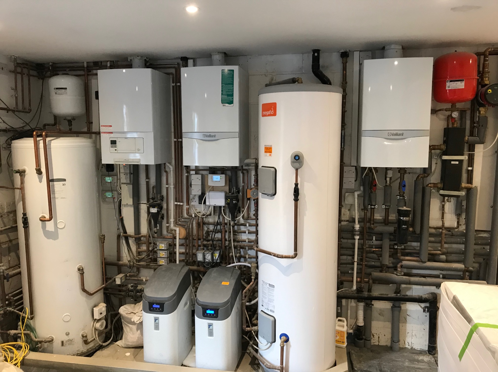 Złożona instalacja CO z kilkoma piecami gazowymi Vaillant, zbiornikami i systemem rur miedzianych w kotłowni. Widoczne filtry do wody i elementy zabezpieczające instalację.